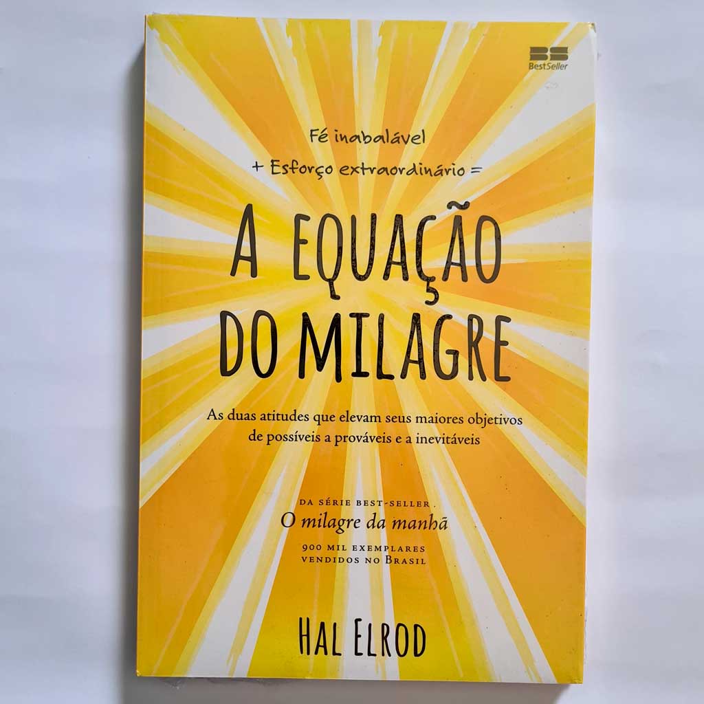  #DescriçãoDaImagem: o livro Equação do Milagre de Hal Elrod está ao centro; o livro tem os escritos em preto e faixas de cores amarelas e brancas saindo do centro da capa. Foto: Shopee Brasil