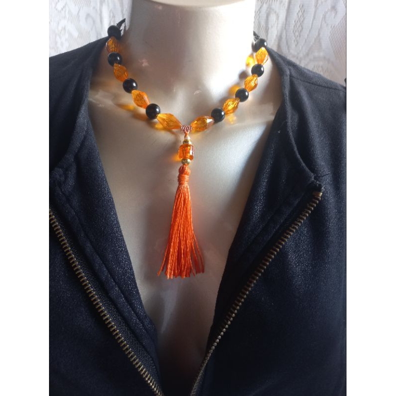 Colar feminino, regulável, de camurça, material metálico, passadores preto e laranja, com pingente tassel laranja.