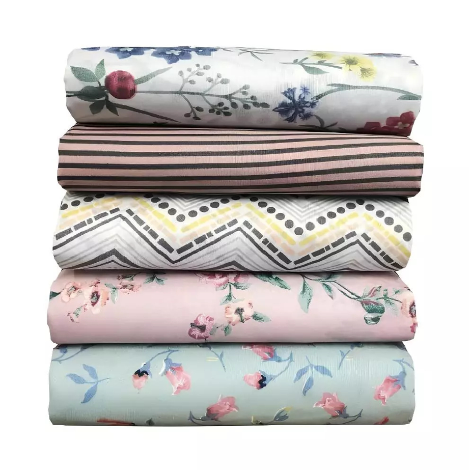 Pilha de cinco lençóis de casal dobrados com estampas variadas, incluindo florais e listrados, com elástico.