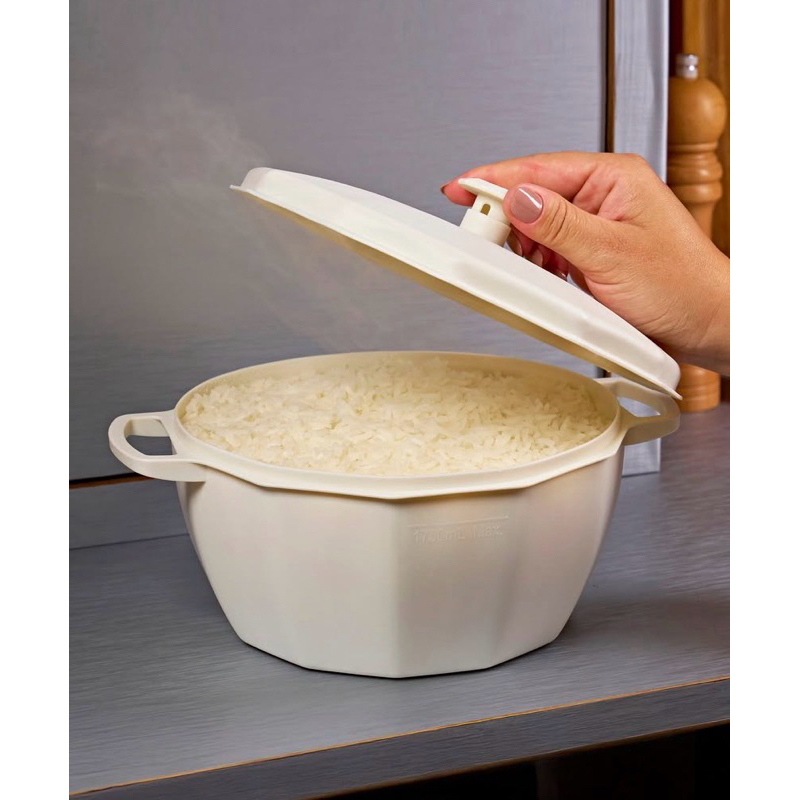 Mão abrindo a tampa de uma panela de plástico bege para micro-ondas contendo arroz cozido, com vapor saindo do recipiente