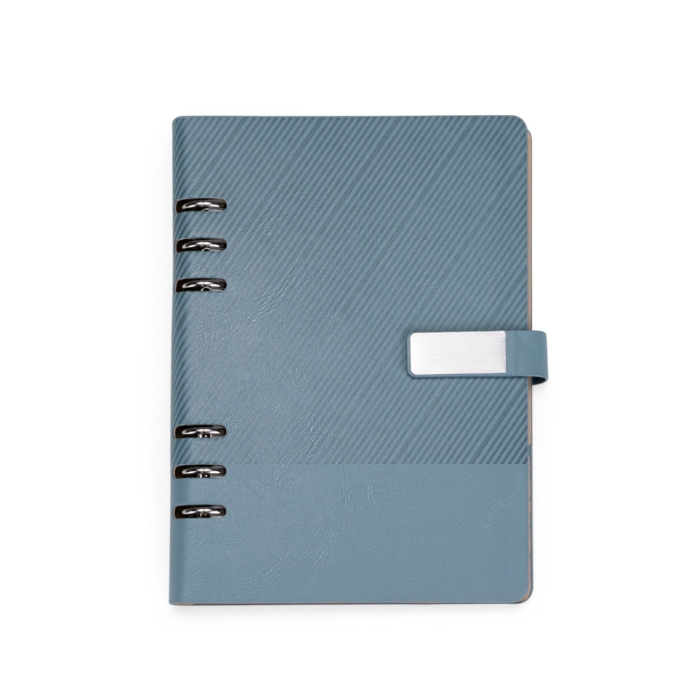 Caderno tipo fichário com capa dura texturizada em couro sintético, fecho magnético e plaquinha metálica fixa à aba. Pos