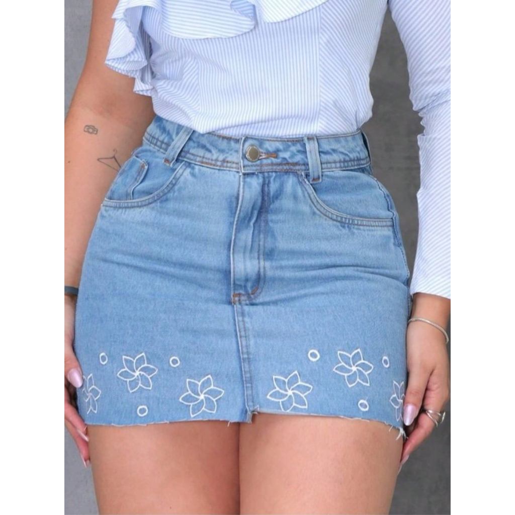Mini saia jeans feminina curta azul claro, corte reto, com bordado floral, zíper e bolsos.Sem elasticidade Saia curta