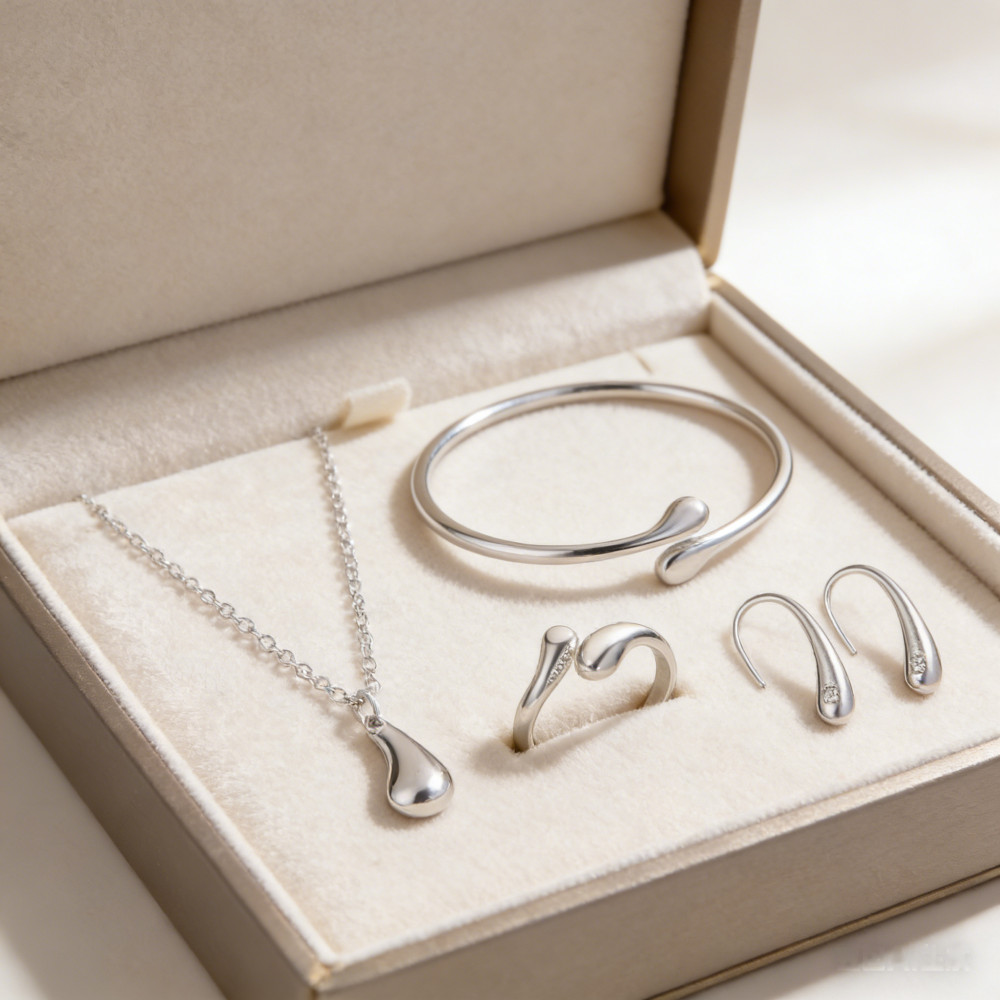 Conjunto de joias em formato de gota, composto por quatro peças em ouro ou prata: brincos, colar, pulseira e anel.