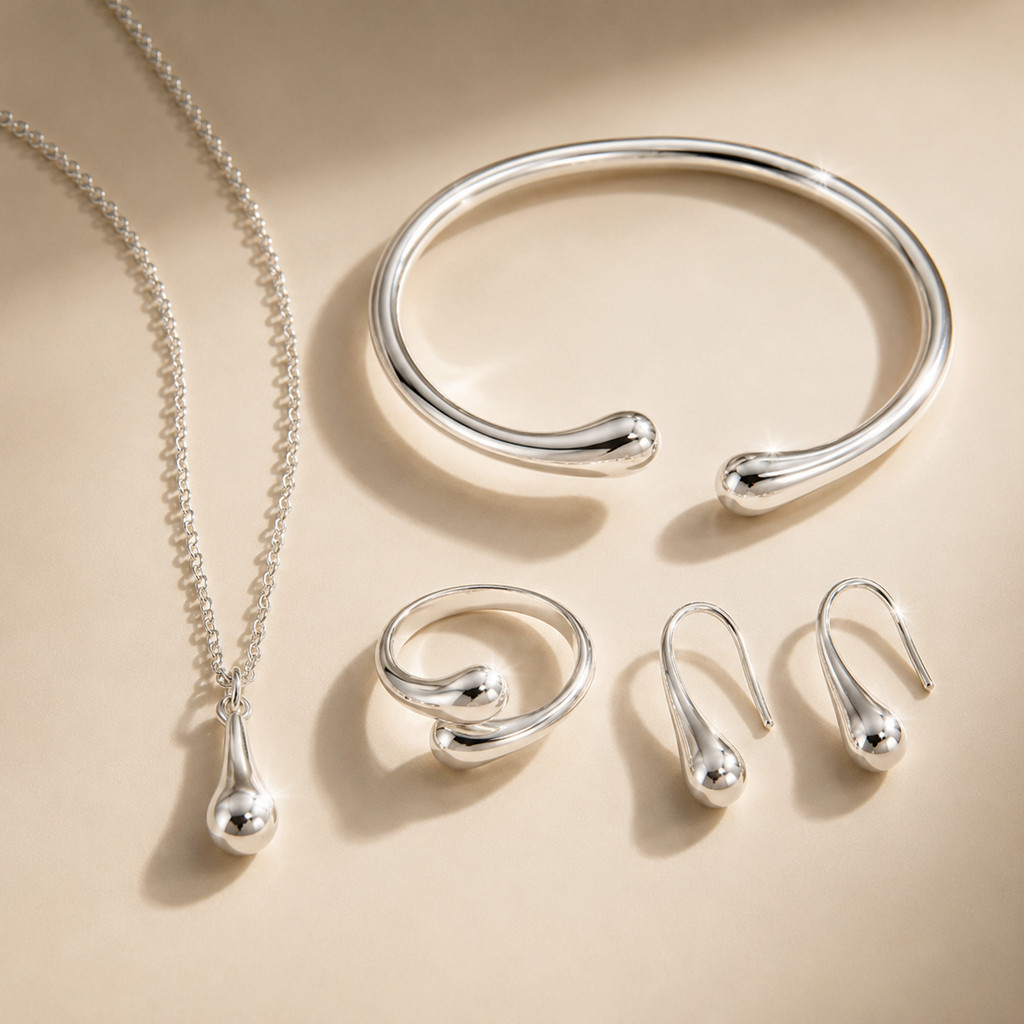Conjunto de joias em formato de gota, composto por quatro peças em ouro ou prata: brincos, colar, pulseira e anel.