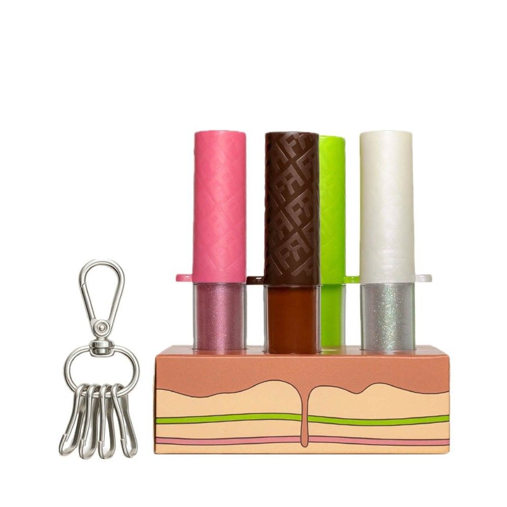 Kit com 4 glosses labiais da linha Fran by Franciny Ehlke Chilli Cake, dispostos em um suporte temático que imita um bolo, acompanhados de um chaveiro metálico.