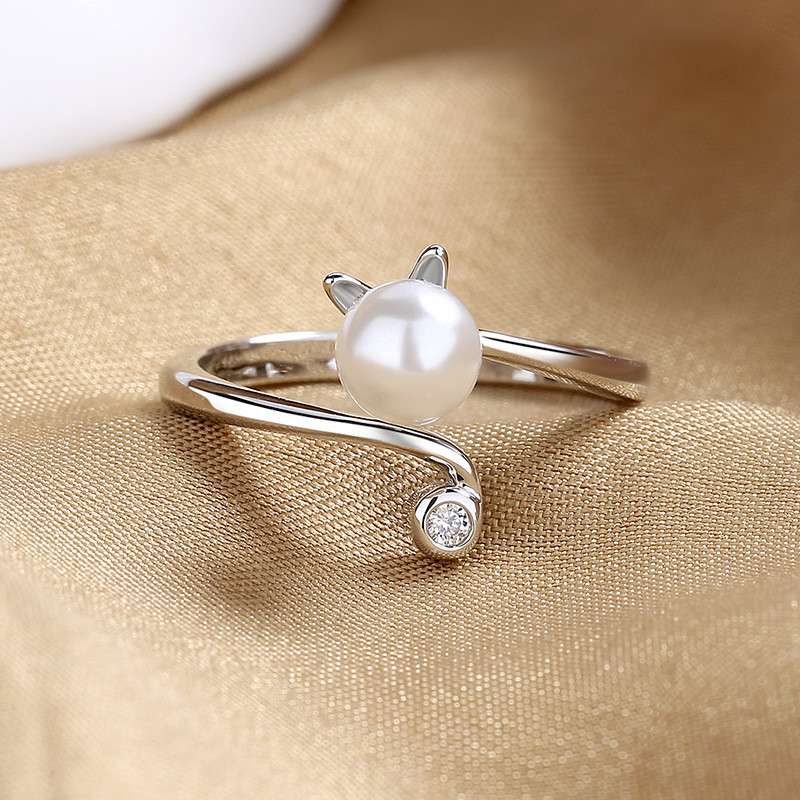 Novo anel feminino, com design inovador e formato único, adornado com um pequeno gato e com base cravejada de pérolas. A