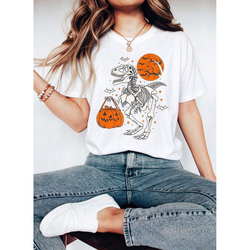 Camiseta Feminina Estampa de Dinossauro Esqueleto T Rex segurando Abóbora Halloween Lua Laranja com Morcegos Divertida F